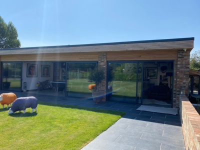 Modern garden outbuilding with brick pillars, flat roof and sliding glass doors; grey tiled patio and green lawn with decorative animal sculptures; part of Glaze Ltd project