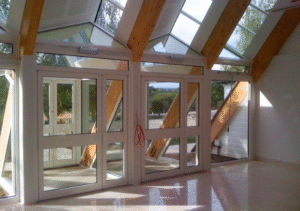 Interior view of glass extension with slanted skylight and exposed wooden beams; large white-framed windows and door units with reflection on polished floor; part of Glaze Ltd project.