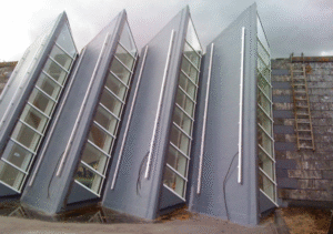 Row of triangular glass rooflight structures leaning against a stone wall at a construction site; part of Glaze Ltd project.